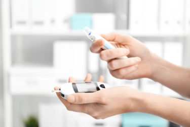 Woman holding digital glucometer and lancet pen on blurred background. Diabetes monitoring