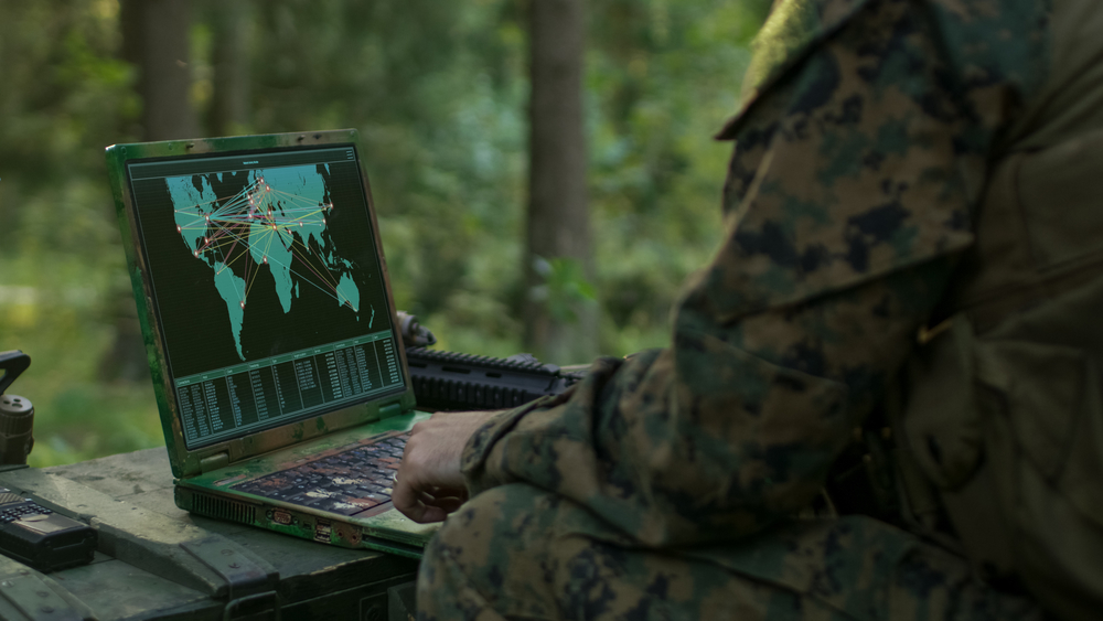 Military Operation in Action, Soldiers Using Military Grade Laptop Use Military Industrial Complex Hardware for Accomplishing International Mission. In the Background Camouflaged Tent on the Forest.